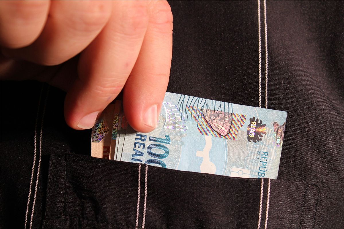 Uma pessoa coloca nota de R$ 100 no bolso depois de começar a investir com segurança