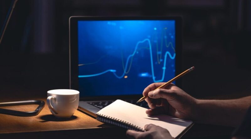 Um jovem segurando o caderno na mesa com lápis na mão que quer começar a investir com segurança em frente ao notebook