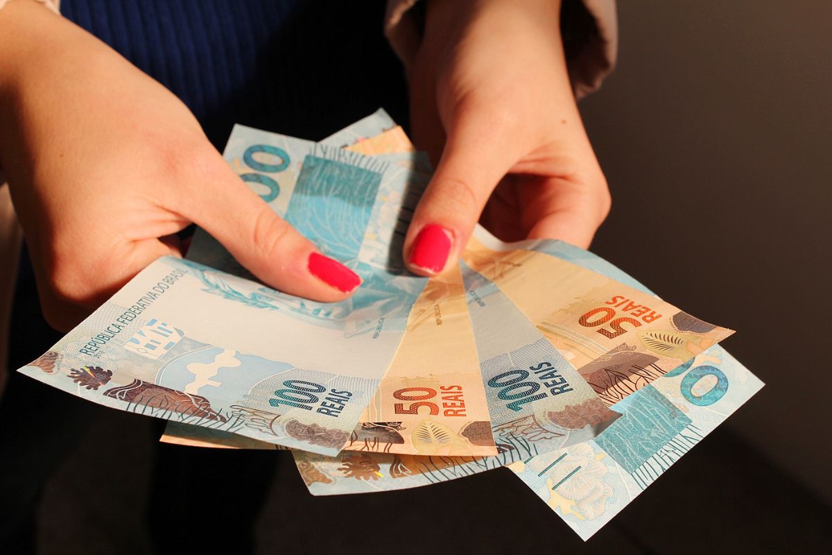 Notas de R$ 100,00 e R$ 50,00 na mão de uma pessoa em busca de renda extra