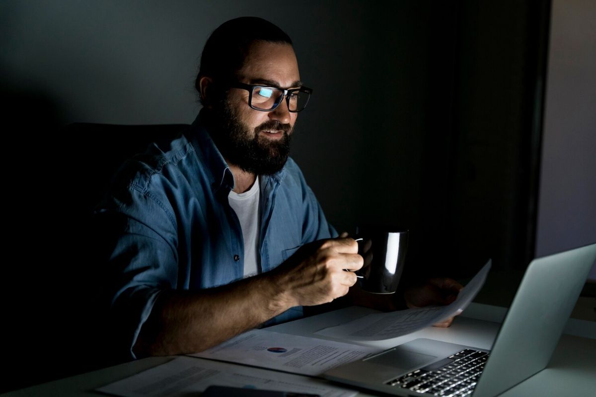 Um rapaz em frente ao notebook com uma xícara na mão