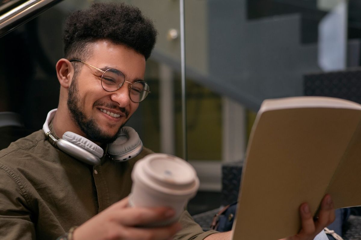 Um rapaz em frente ao notebook com um copo na mão em busca de renda extra