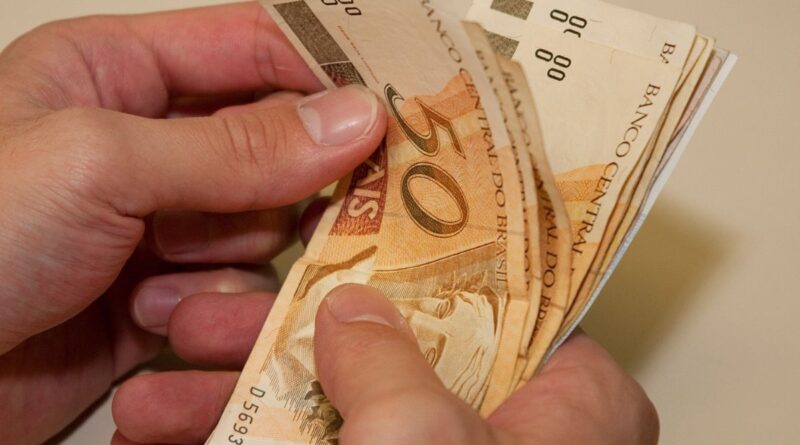 Notas de R$ 50,00 na mão de uma pessoa em busca de renda extra