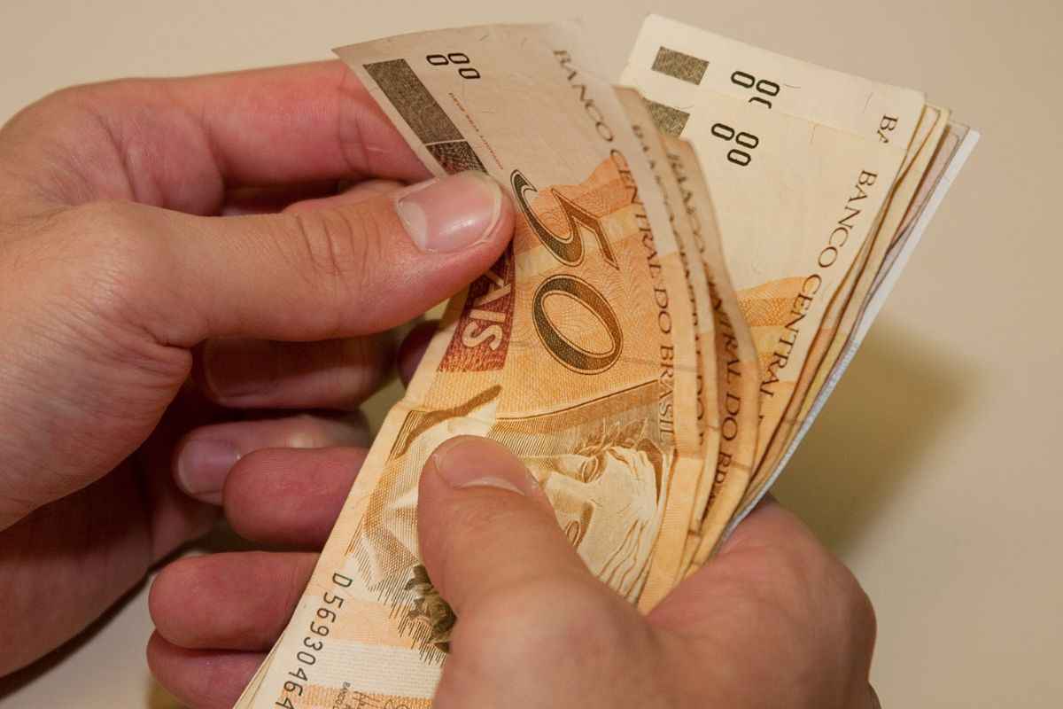 Notas de R$ 50,00 na mão de uma pessoa em busca de renda extra