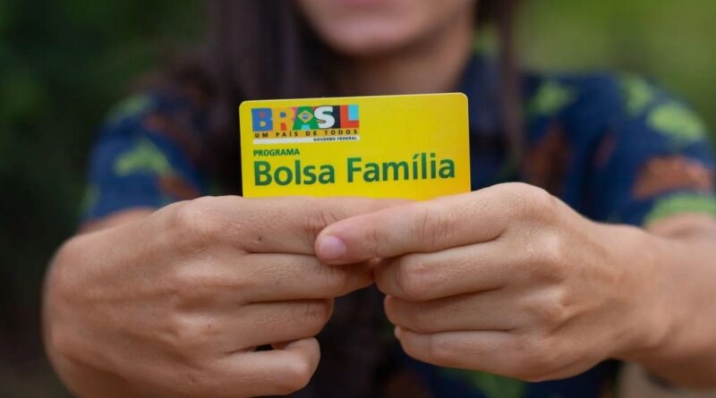 Uma mulher sorri com o cartão do Bolsa Família
