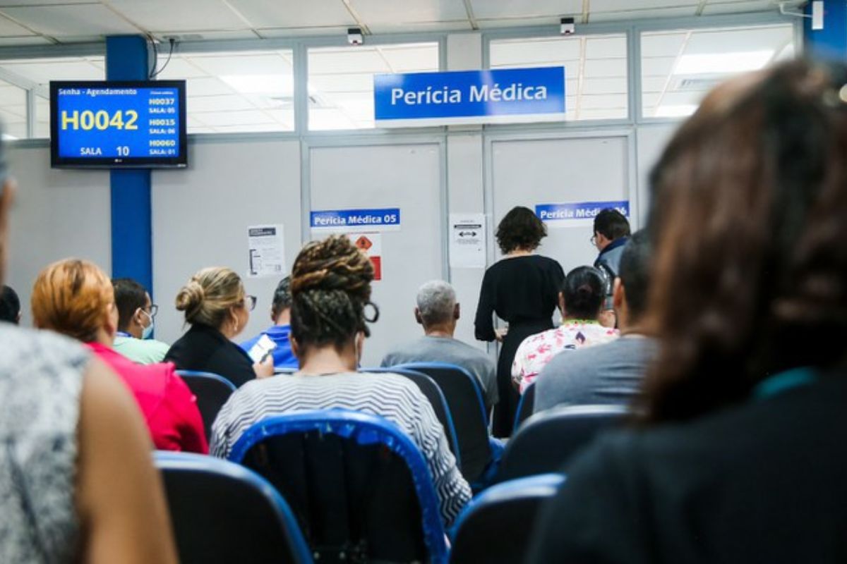 Pessoas sentadas esperando na fila do benefício